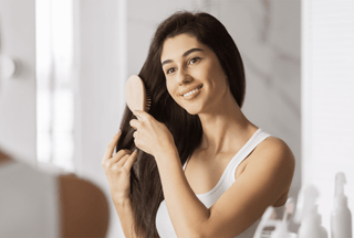 Happy young woman with thick brown hair brushes her hair in the bathroom mirror