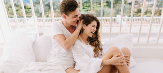Man in white runs his fingers through a girl in white’s healthy hair on the couch