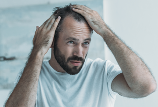 middle aged man with beard looking at his hair loss in a mirror