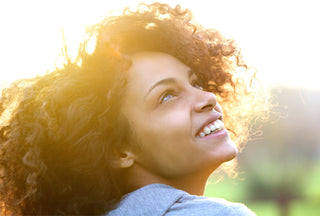 Young woman with naturally curly natural hair smiling and looking up during sunset