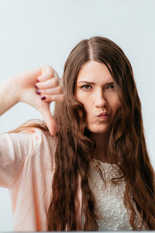  Chica morena de cabello largo con el cabello graso que muestra el pulgar hacia abajo aislado sobre un fondo blanco