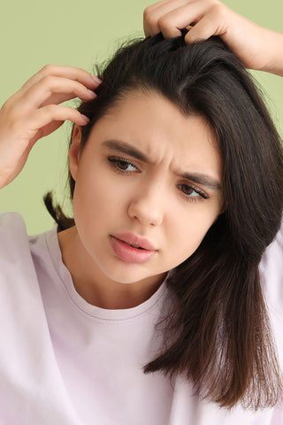 Mujer joven con picazón en el cuero cabelludo y problema de caspa escamosa examinando su cabello sobre fondo verde