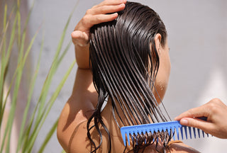 Modelo femenina joven colocando una mascarilla refrescante en su cabello largo húmedo con un peine de madera