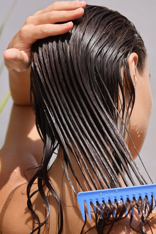 Modelo femenina joven colocando una mascarilla refrescante en su cabello largo húmedo con un peine de madera