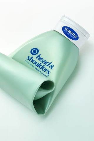 Botella doblada de champú ecológica verde claro vacía y rizada sobre un fondo blanco