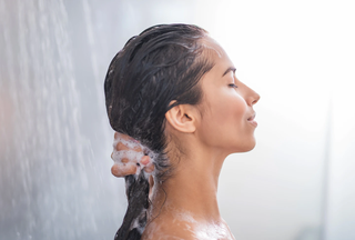 A tan-skinned woman rinses Head & Shoulders shampoo, the best shampoo for dandruff, out of her black hair in the shower.