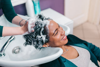 hairdresser washing the hair of an african-american woman in the seat of a hair salon