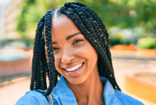 Joven afroamericana con trenzas sonriendo feliz tomándose una selfi con su cámara en el parque.