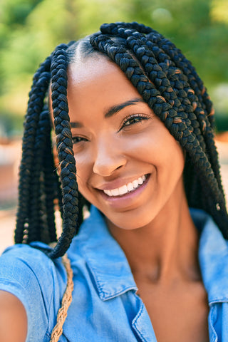 Joven afroamericana con trenzas sonriendo feliz tomándose una selfi con su cámara en el parque.